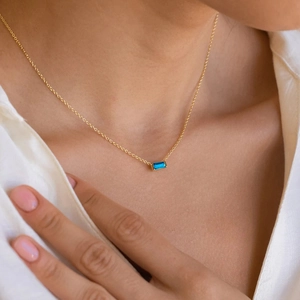 Elegant gold necklace with a rectangular blue gemstone pendant worn on a white shirt