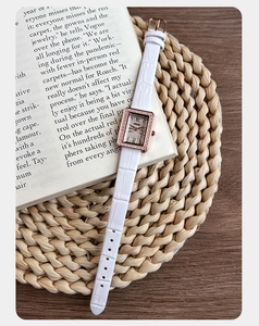Dettaglio dell'orologio rettangolare in oro rosa su libro con cinturino bianco
