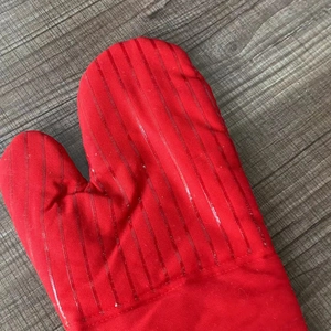 Detailed view of red cotton oven mitt with anti-slip silicone pattern on a wood background