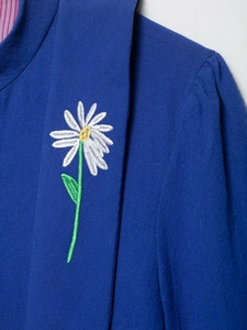 Close-up of white daisy embroidery on navy blue textured casual hooded jacket fabric