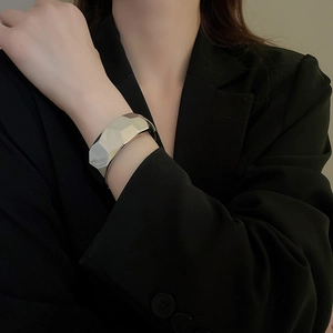 Detail view of irregular geometric silver cuff bracelet on model wearing black suit jacket