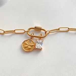 Close-up van een goudkleurige armband met vlindermunt en vierkante zirkoon hanger