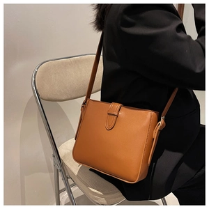 Detail shot of a brown leather crossbody bucket bag on a model wearing a black blazer