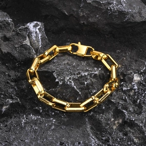 Detailed shot of a gold stainless steel chain bracelet on a black textured rock surface