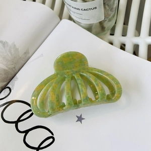 Détail d'une pince à cheveux en acétate marbré vert et jaune sur un magazine