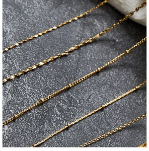 Detailed close-up of various golden titanium steel necklaces on a dark textured surface