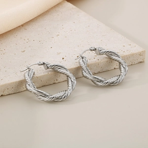 Detailed close-up of twisted silver hoop earrings on a textured stone surface