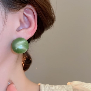 Close-up of a green round resin stud earring with glossy finish worn on a model