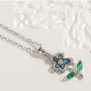 Close-up of silver necklace with abalone shell flower pendant and green gemstone leaves