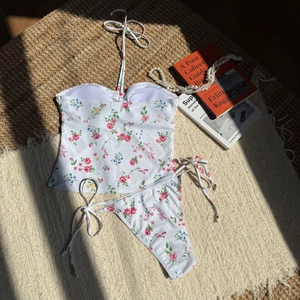 Detailed flat lay of a white floral bikini with pink rose print on a woven texture mat