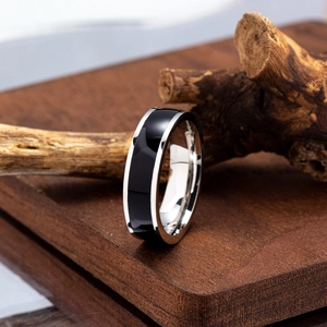 Macro shot of striped titanium steel ring with black enamel drip on dark wood base