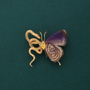 Detailed shot of exotic golden snake brooch with purple and brown embroidery butterfly