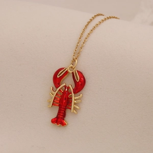 Macro view of gold necklace with a vibrant red enamel lobster pendant and fine link chain