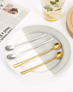 Close-up of gold and silver long-handle stainless steel mixing spoons on a ceramic plate