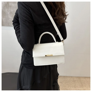 Minimalist white leather handbag with gold metal clasp shown on female model shoulder