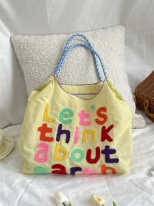 Detail of yellow canvas tote bag with towel embroidery text and blue plaid handle
