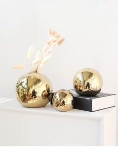 Detailed view of three sizes of golden mirror finish spherical ceramic vases on a desk