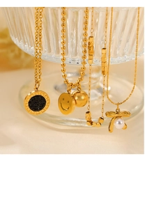 Detail of four gold-plated titanium necklaces with various pendants on a glass bowl