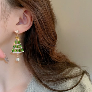 Detail shot of a Christmas tree earring with green rhinestones and a white pearl drop