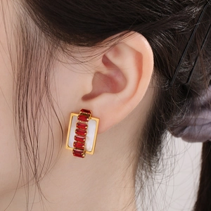 Detail of gold rectangular earrings with red zircon stones worn on a model's ear
