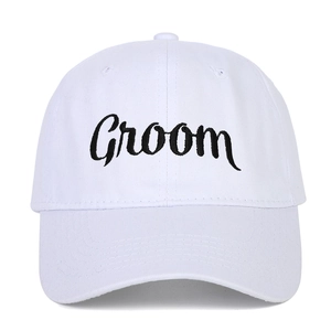 Detailed view of the Groom cursive embroidery on the white cotton baseball cap
