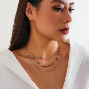 Close-up of triple-layered gold chain necklace with colorful enamel floral details