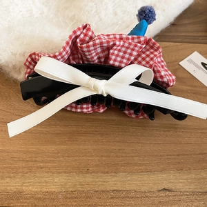 Detail of red gingham fabric hair claw clip with large white silk bow and plush pom-pom