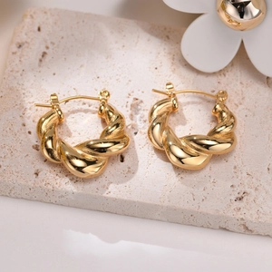 Detail of twisted gold hoop earrings with polished finish on a beige stone base