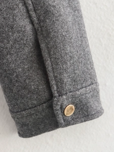 Detail der dunkelgrauen Tweed-Jackenmanschette mit einem polierten goldenen Metallknopf