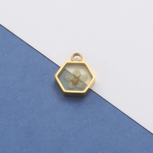 Close-up of hexagonal gold pendant with dried flowers and resin seal on blue background