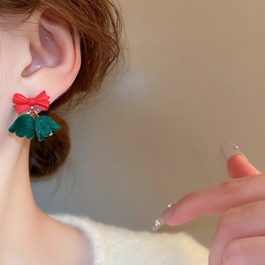 Close-up of Christmas earrings with red bows and green velvet bells worn by a model