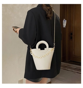 Chic beige bucket bag with round handle and thick acrylic chain detail shown on a model