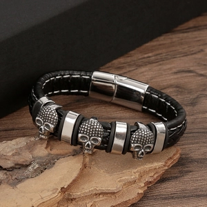 Detail of black braided leather bracelet featuring silver metal skulls on rustic tree bark