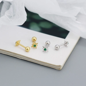 Macro view of gold and silver star stud earrings with a green gemstone on white paper