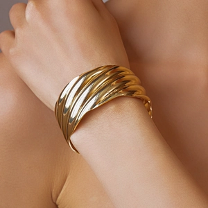 Close-up of golden wide cuff bracelet with artistic wavy texture on a model's wrist