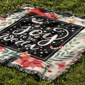 Detail of woven Christmas throw blanket with Joy to the World text and fringe on green grass