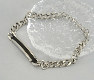 Détail du bracelet gourmette argenté avec plaque d'identification noire et fermoir