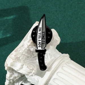 Detail of dagger enamel pin with Don't Tell Me To Smile text on white roman pillar