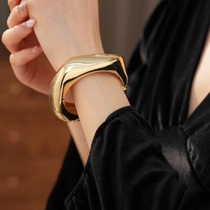 Detailed view of chunky golden irregular wavy metal cuff bracelet with mirror finish