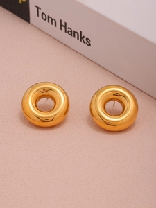 Detailed view of hollow gold-plated hoop earrings on a soft pink background with a book