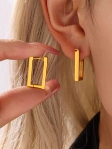 Detailed view of rectangular gold geometric hoop earrings worn on ear and held by hand