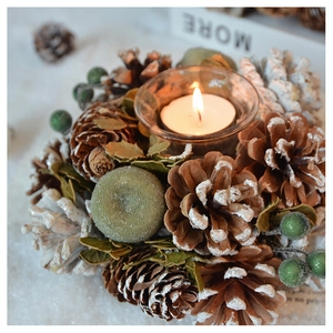 Close-up of pine cones and green berries surrounding a glass candle cup for Christmas