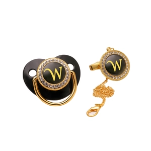 Detail view of black and gold baby pacifier with letter W and rhinestone chain clip