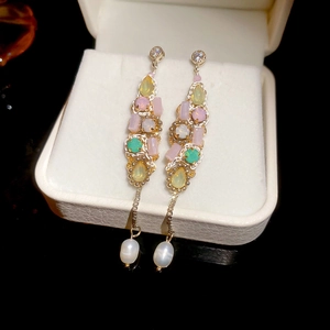 Macro detail of gold tassel earrings with pink and green gemstones in a white velvet box