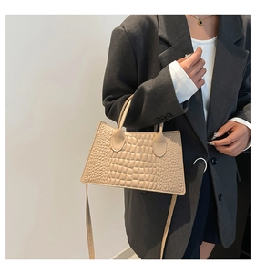 Detail view of beige crocodile pattern handbag with trapezoid shape and top handle