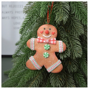 Gingerbread man ornament with red bow tie hanging on green Christmas tree branches