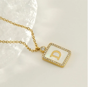 Macro detail of 18K gold-plated square letter D pendant with shell base and rhinestones
