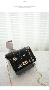 Close-up of black crossbody bag with pink floral embroidery and golden metal chain strap