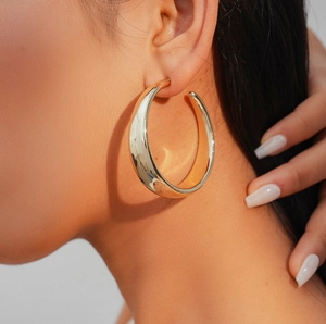 Close-up of model wearing wide C-shaped gold hoop earrings with a polished metallic finish