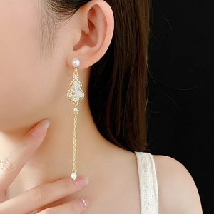 Detail view of gold gourd tassel earrings with pearls and white floral accents on model